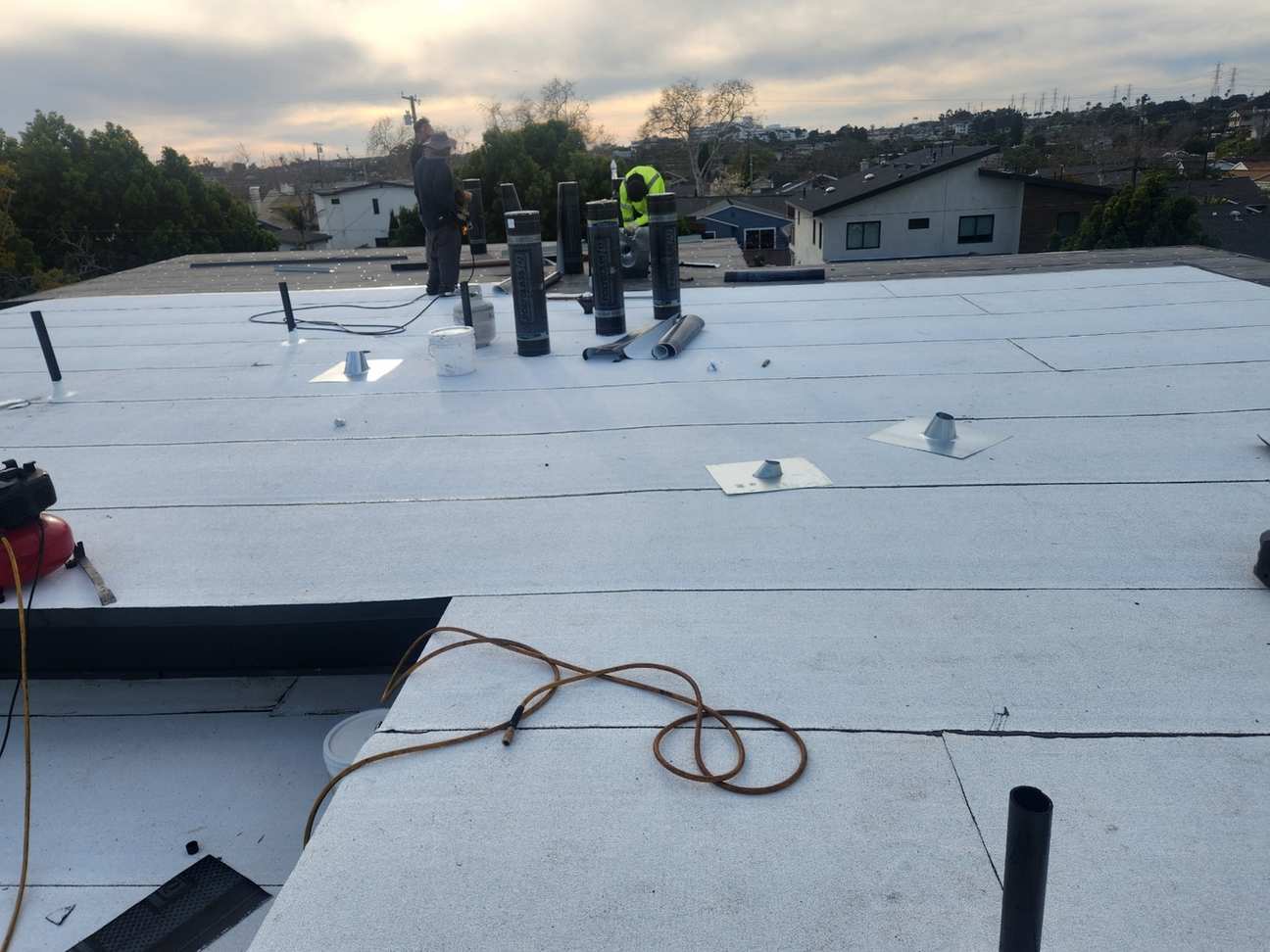 Roofing crew, membrane rolls and pipe flashing on a low-slope roof